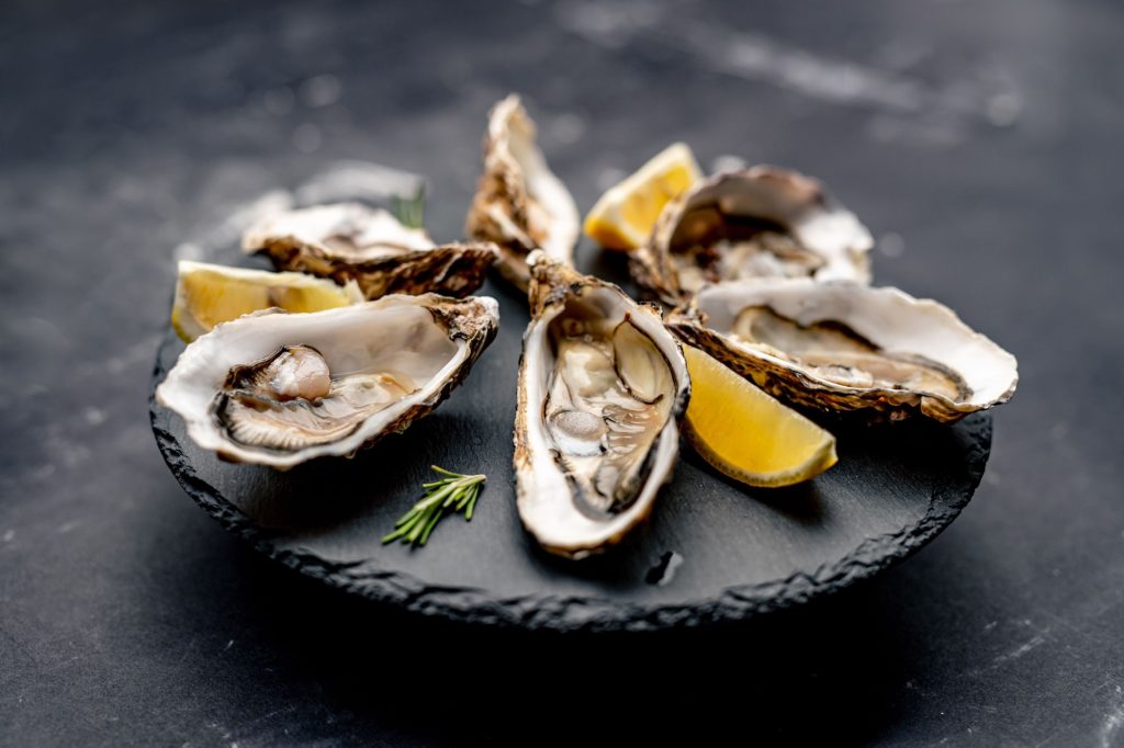 Oysters with lemon served on black round platter. Luxury delicatessen seafood