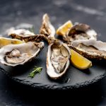 Oysters with lemon served on black round platter. Luxury delicatessen seafood