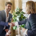 Smiling businessman shaking hands with colleagues in modern office. Professional greeting, successful partnership. Corporate environment, positive business interaction, teamwork concept.