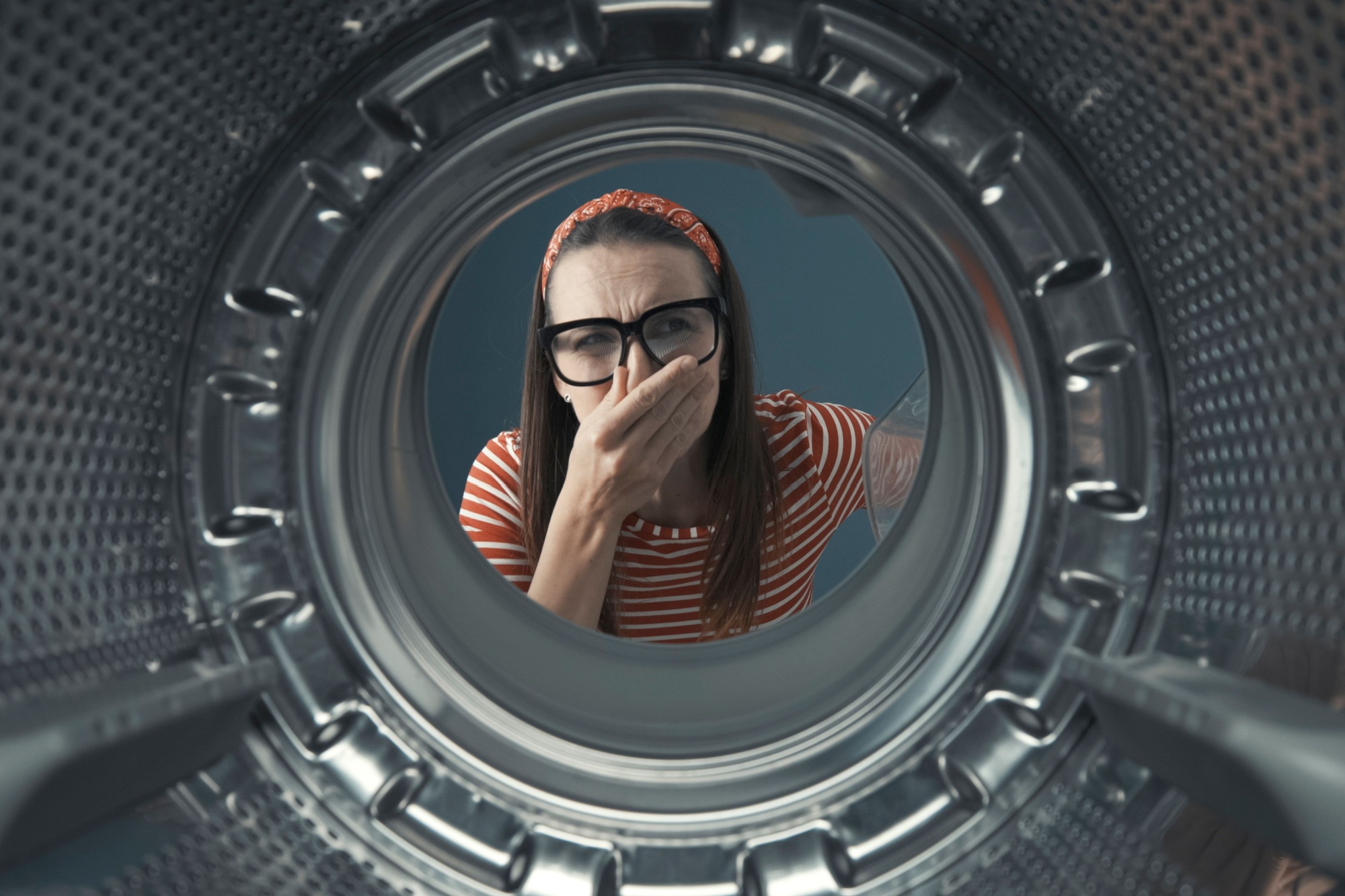 Disgusted woman looking into her smelly washing machine, she is holding her nose, point of view shot