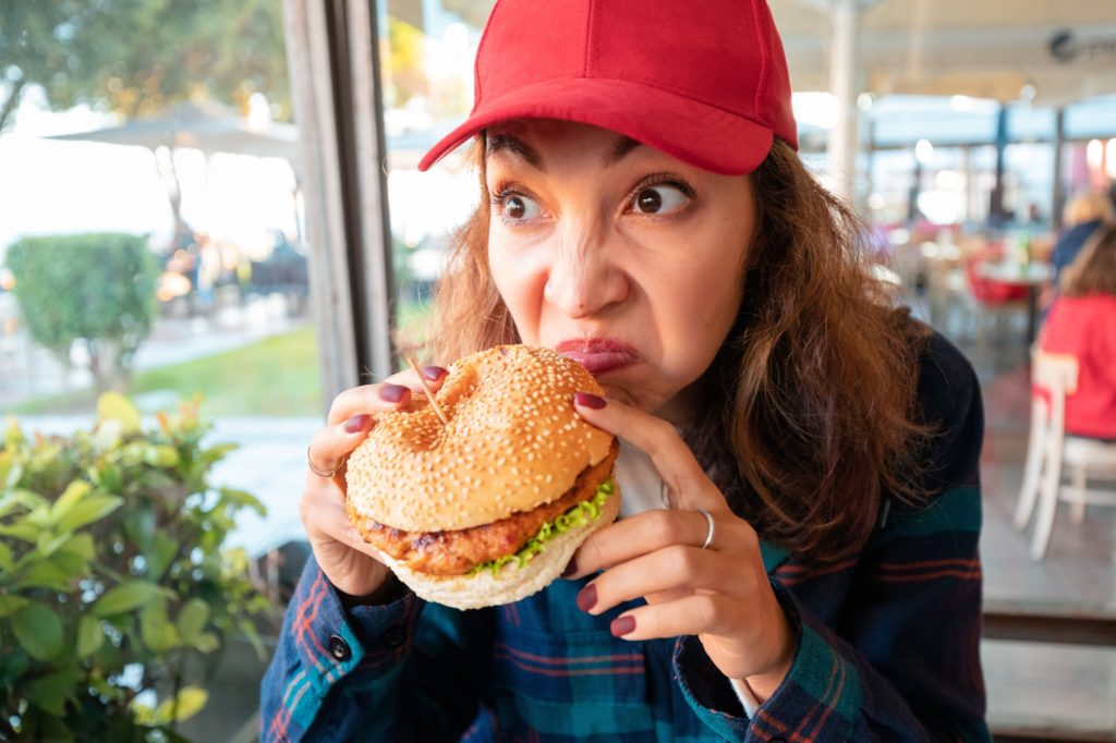 A woman sniffs burger in a cafe with disgust on her face. The concept of spoiled food and poisoning in catering restaurant