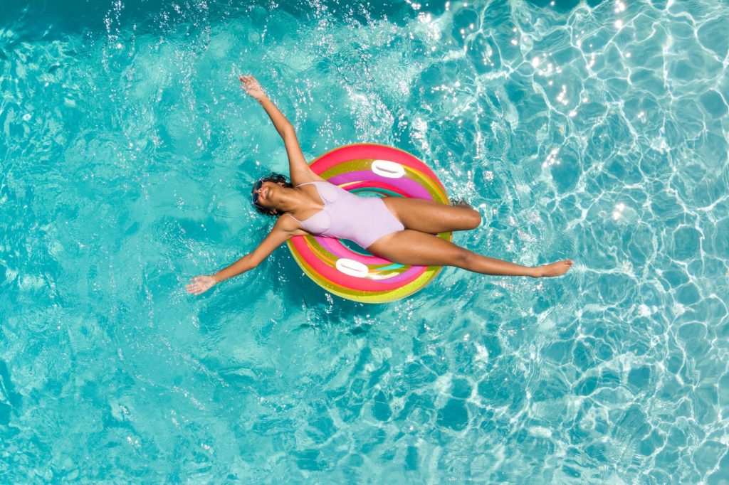 Teenage biracial girl enjoys a sunny day in the pool. She relaxes on a colorful float, embracing the joy of summer.