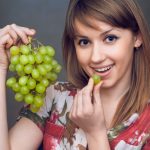 The beautiful girl is eating the green grapes