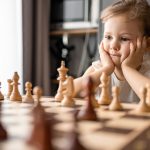 Little girl playing chess at the table in home kitchen. The concept early childhood development and education. Family leisure, communication and recreation. High quality photo