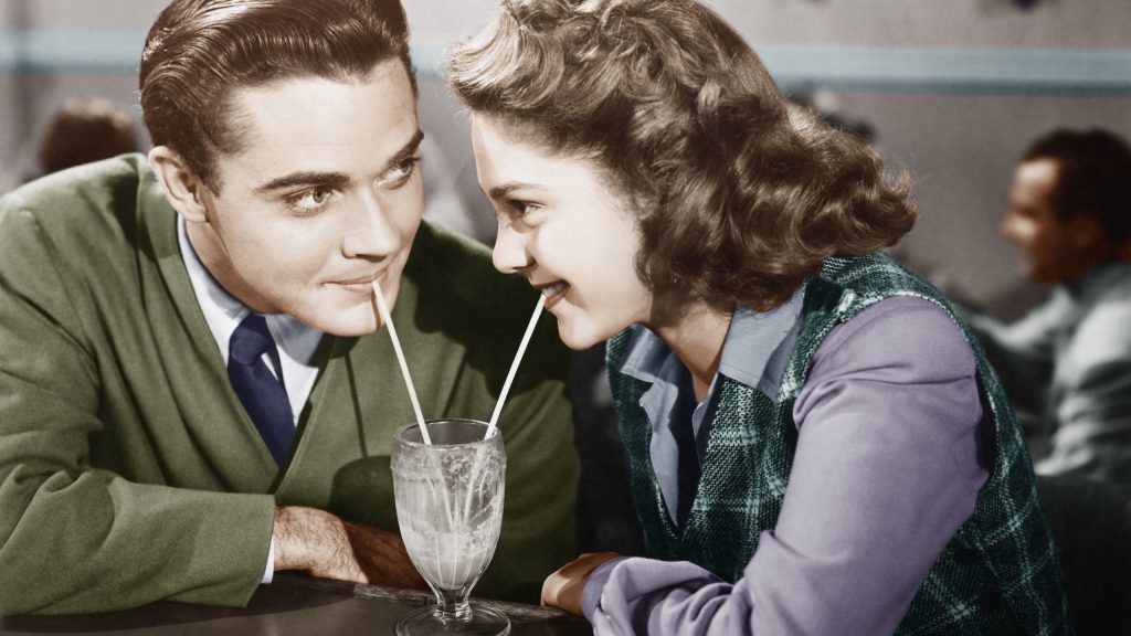 Couple in a restaurant looking at each other and sharing a milk shake with two straws