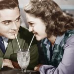 Couple in a restaurant looking at each other and sharing a milk shake with two straws