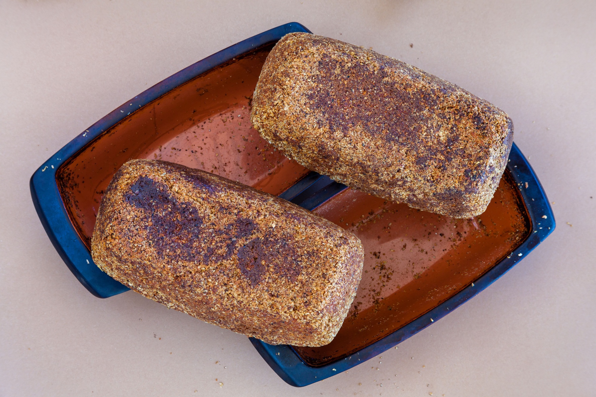 Bread loafs put upside-down for cooling. Freshly made multigrain wheat bread on clay rectangular forms. Crumbs and bran around. Flat lay.