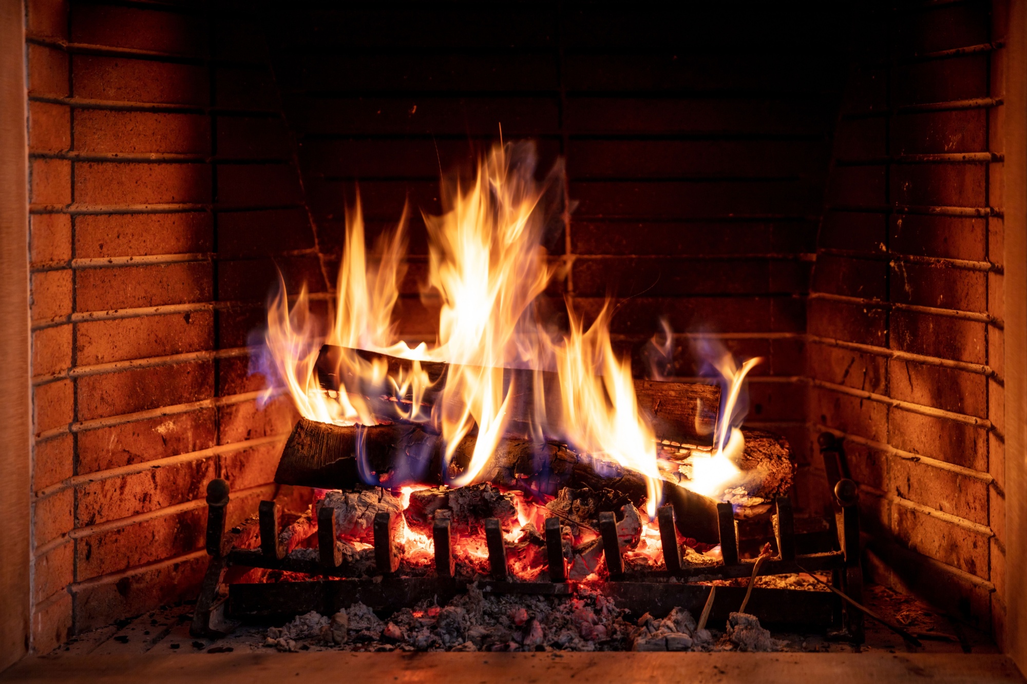 Fireplace burning firewood. Bonfire, fire flames on wood logs, bricks background. Cozy room interior at Christmas. Winter holidays relaxation and warm home