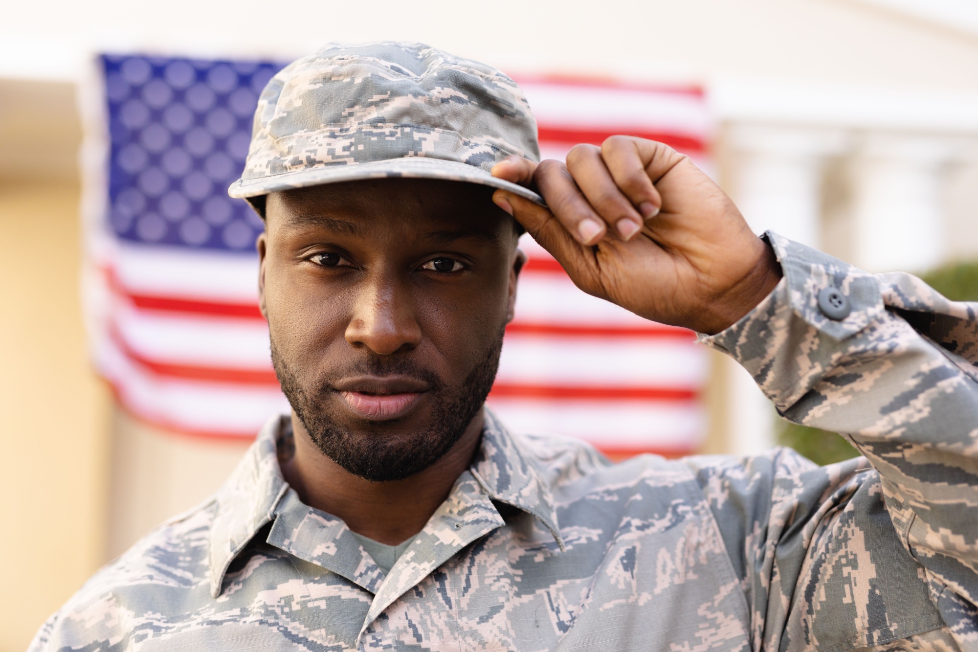 Portrait of confident male african american army soldier wearing cap and uniform against flag. patriotism and identity, unaltered.