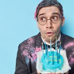 Stunned impressed brunet man looks shocked away going to blow candes on birthday cake thinks about wish dressed in festive clothes isolated ver blue background blank copy space for promotion