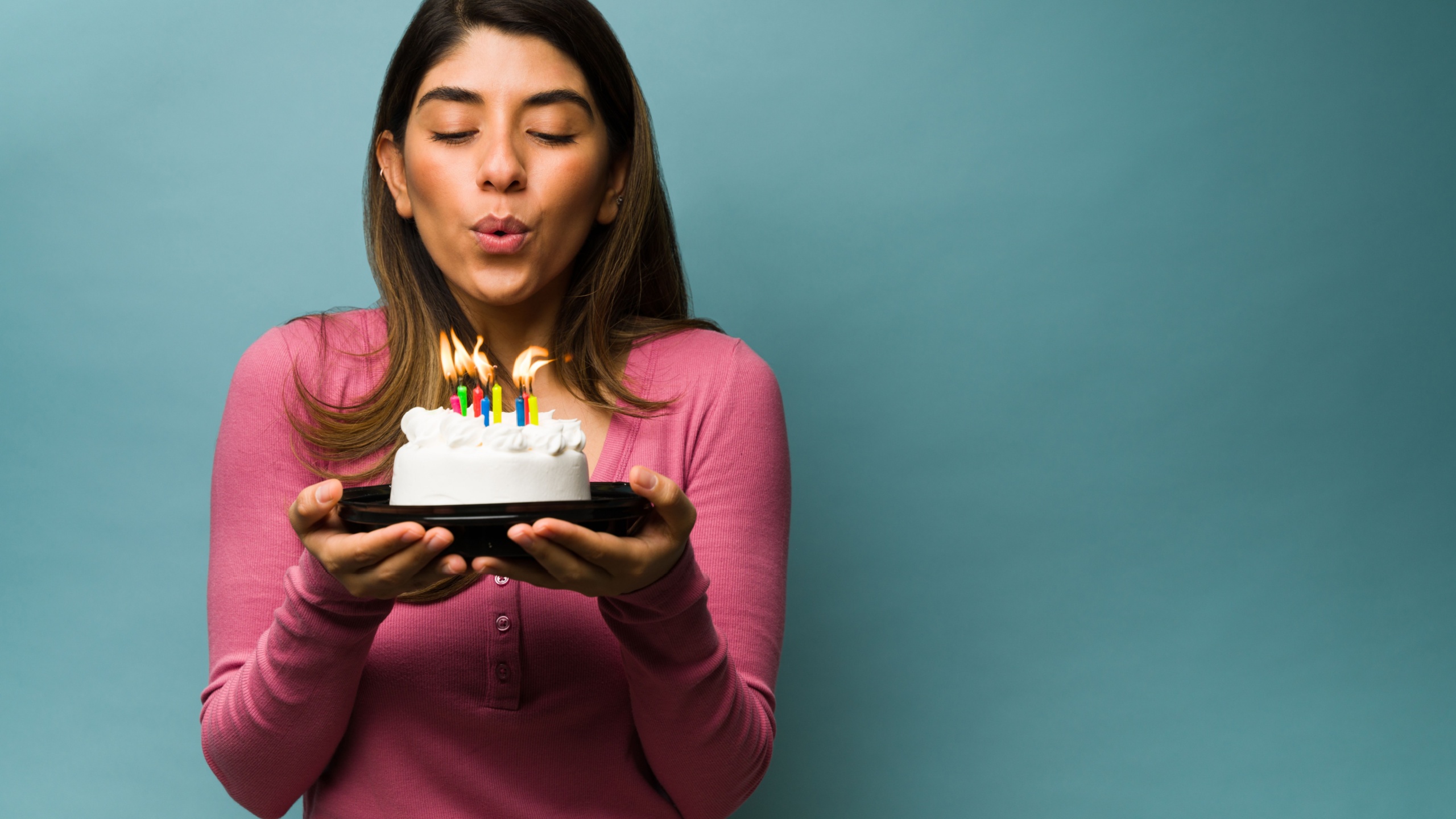 Blowing the birthday candles. Attractive young woman making a wish while holding a delicious cake next to copy space