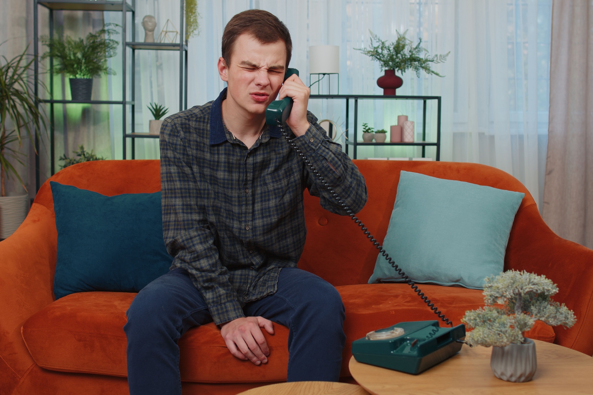 Portrait of teenager man making wired telephone conversation with friends sitting call on couch at home in room. Happy excited young guy enjoying old-fashioned retro phone from 90s talking indoors