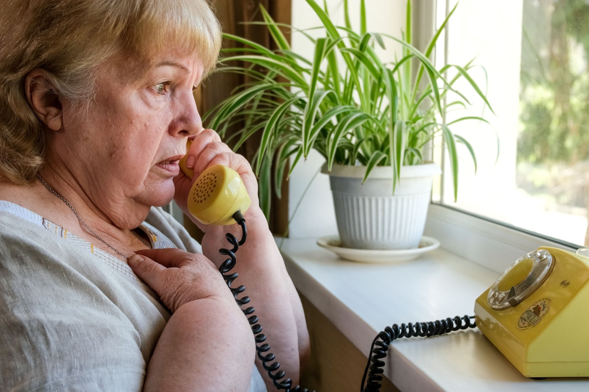 Old woman receives phone call from a scammer. Frightened grandmother talking on an old disc phone