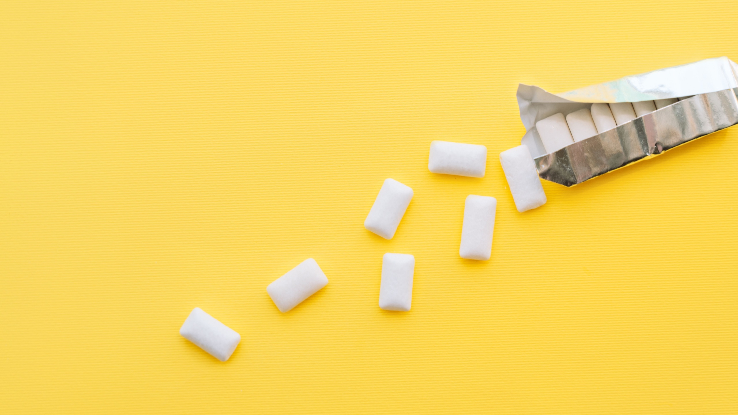 White chewing gum pads spilled out of a foil package on a yellow background.