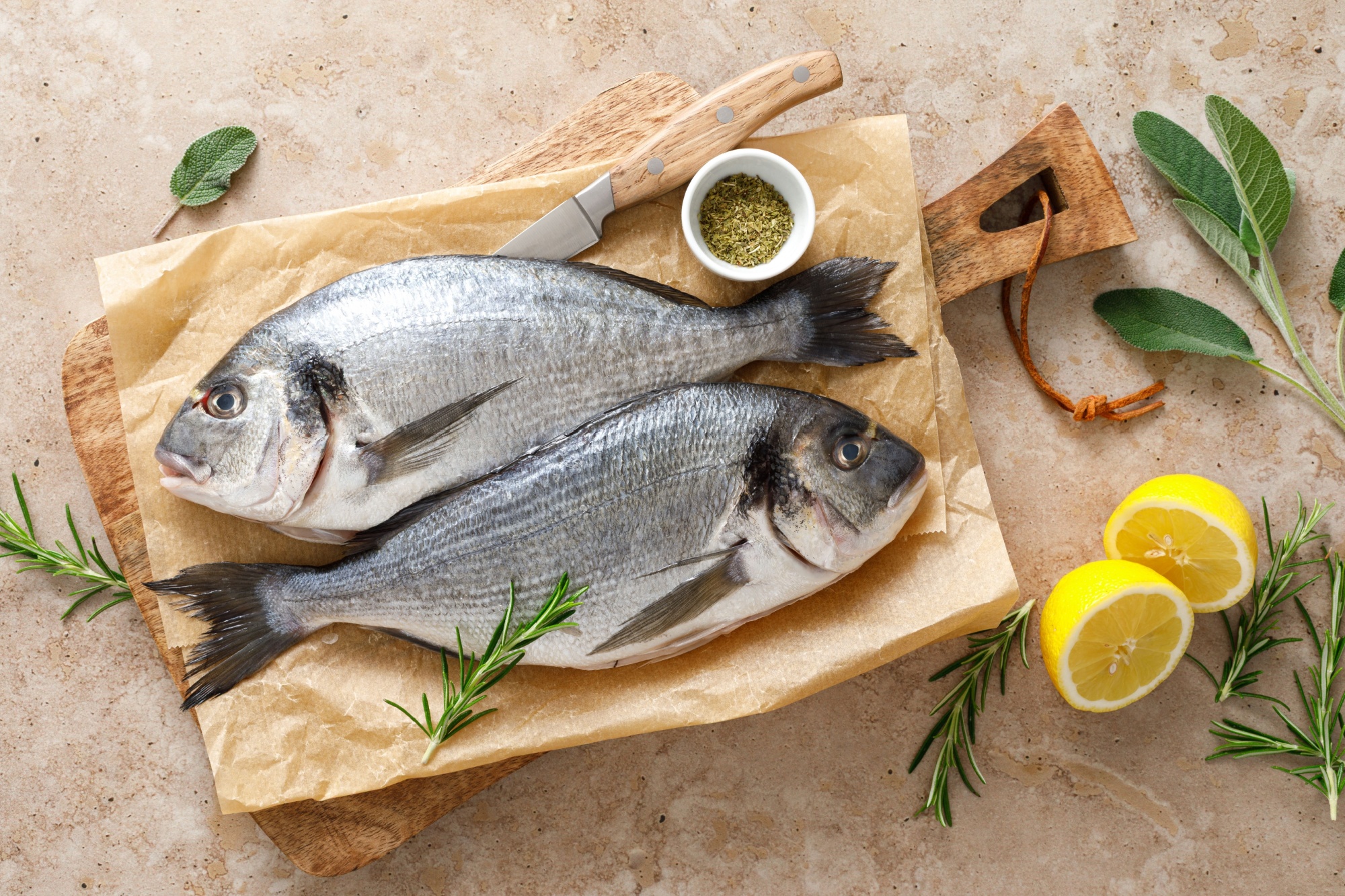 Fresh raw sea bream fish or dorado fish with lemon and herbs, top view