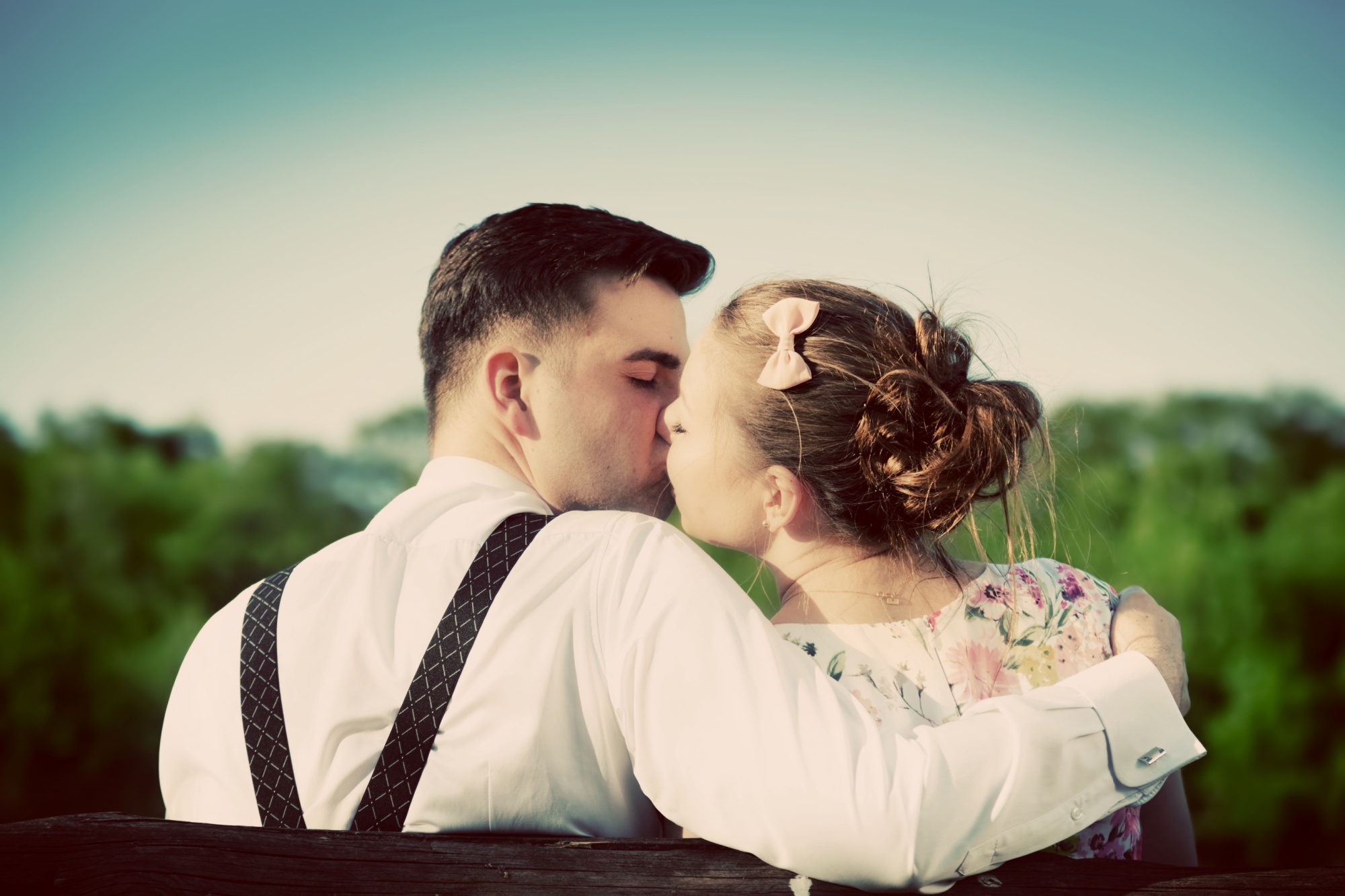 Young couple in love kissing on a bench in summer park. Man wearing shirt with suspenders. Happy future, marriage concepts. Vintage