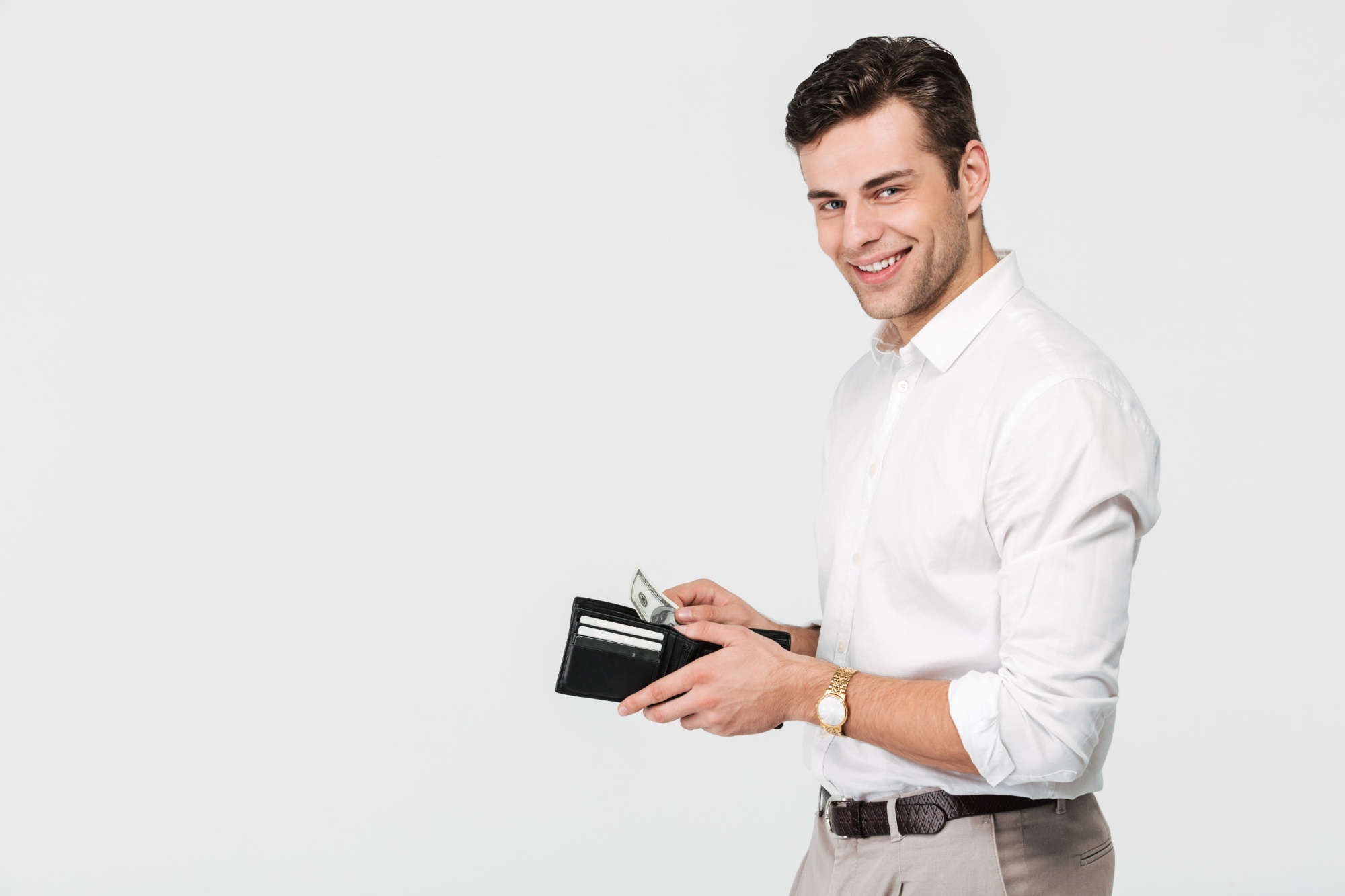 Portrait of a confident smiling man holding wallet full of money and looking at camera isolated over white background