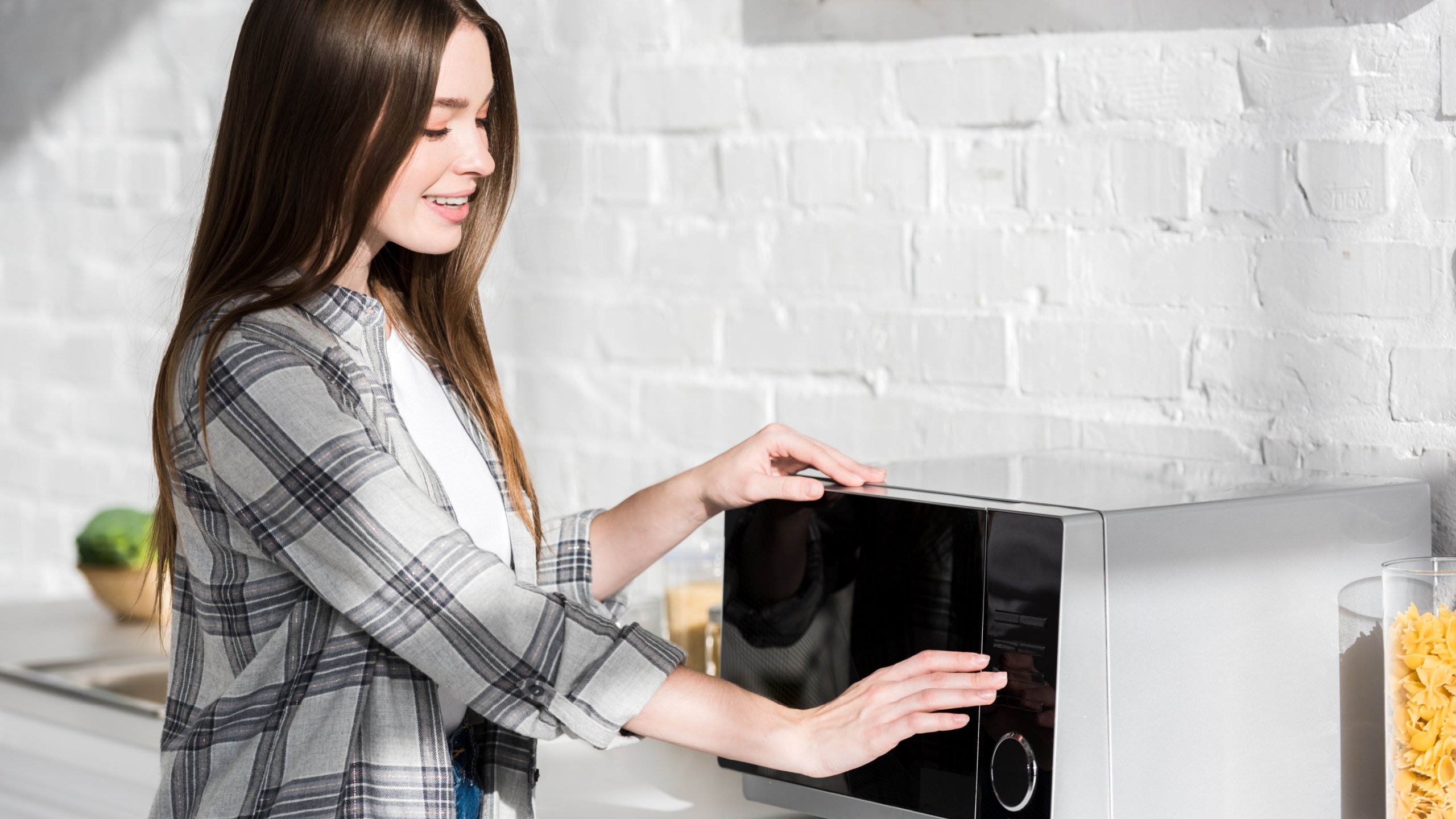 Smiling and attractive woman in shirt using microwave in kitchen