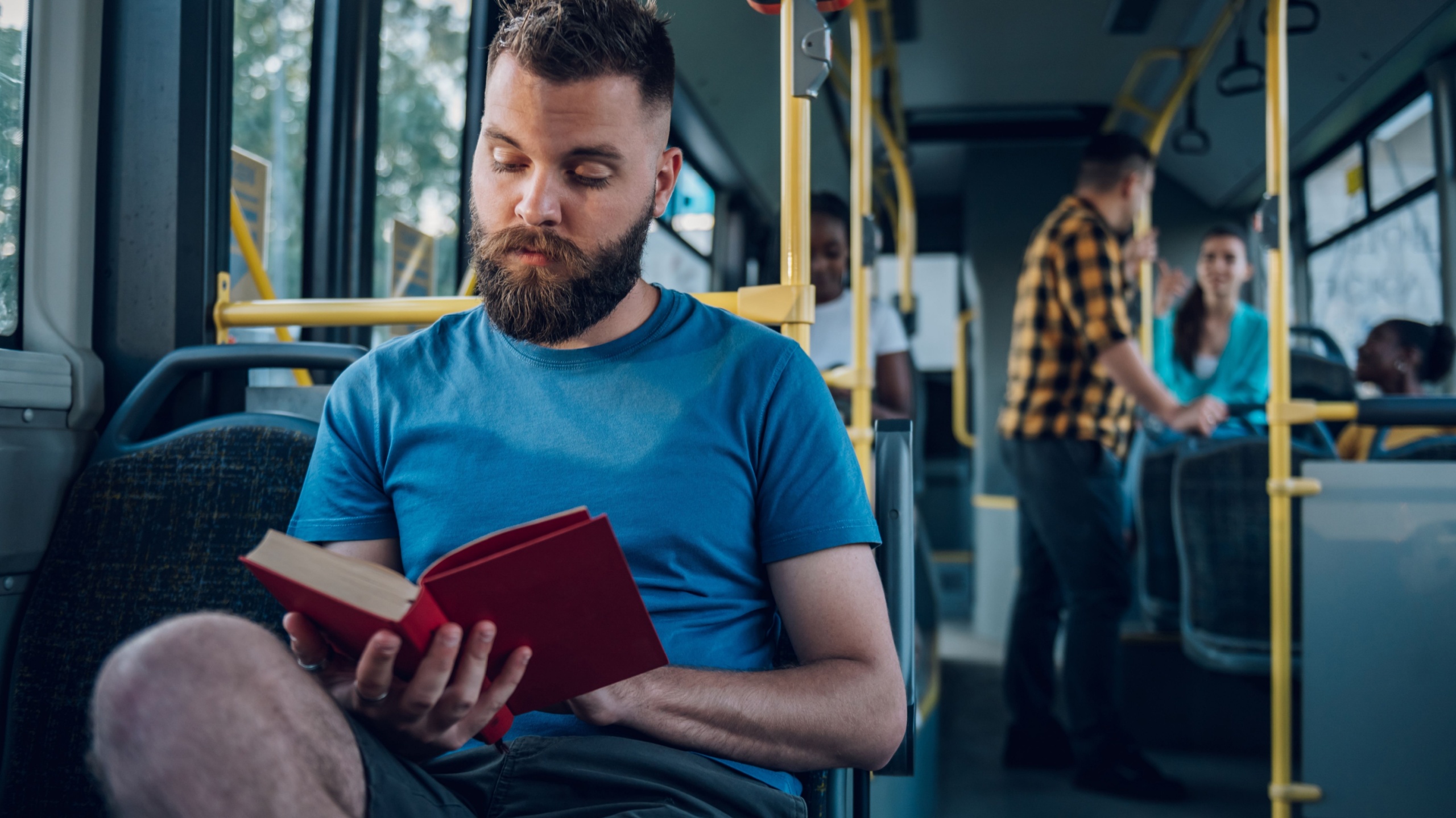 Portrait of a man sitting in a bus and reading a popular fiction book. Everyday life and commuting to work by public transportation. Man is reading a novel and enjoying his ride.