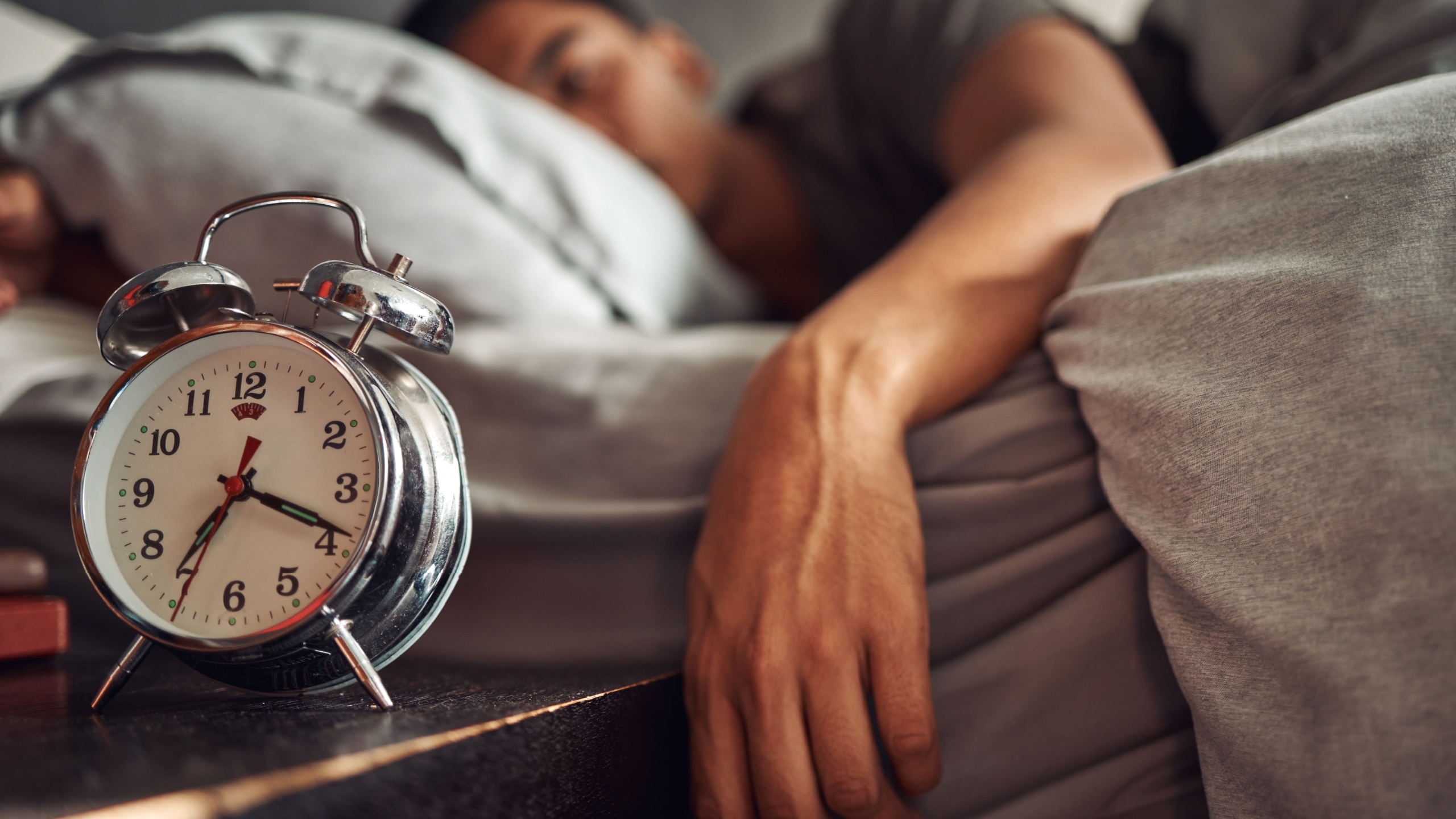Alarm clock, relax and man sleeping in the bed of his modern apartment in the morning. Lazy, resting and closeup of a timer bell with a male person taking a nap and dreaming in bedroom at his home.