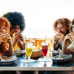 Multiethnic group of friends having meal at 80s vintage diner restaurant - Multiracial young people bonding and having fun, eating in an american fast food burger house