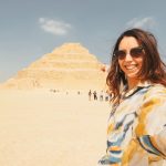 Young woman taking a selfie in the saqqara desert in front of the step pyramid of djoser, an important archaeological site in egypt