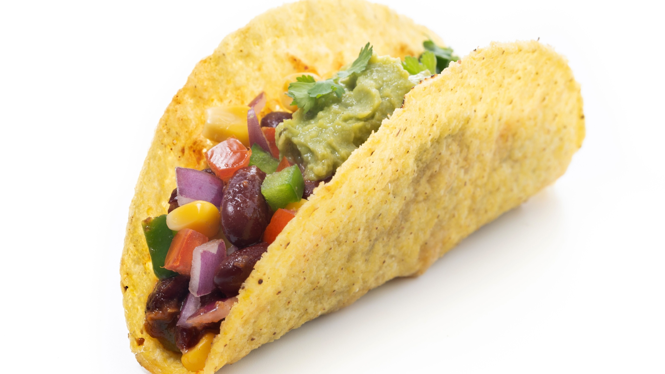 Close-up of a colorful vegetarian taco with kidney beans, corn, diced red onion, bell peppers, cherry tomatoes, fresh guacamole isolated on white background