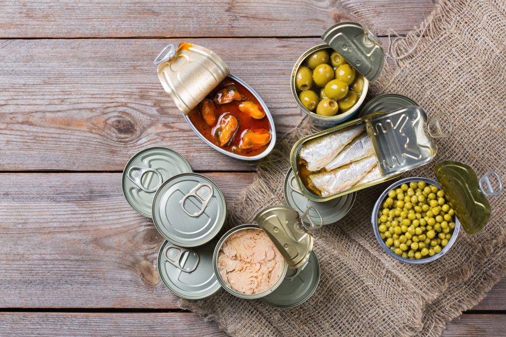 Assortment of different canned preserved vegetables, meat, fish, seafood in tin cans on a wooden table. Non-Perishable goods, food, donations concept. Flat lay top view background