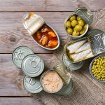 Assortment of different canned preserved vegetables, meat, fish, seafood in tin cans on a wooden table. Non-Perishable goods, food, donations concept. Flat lay top view background