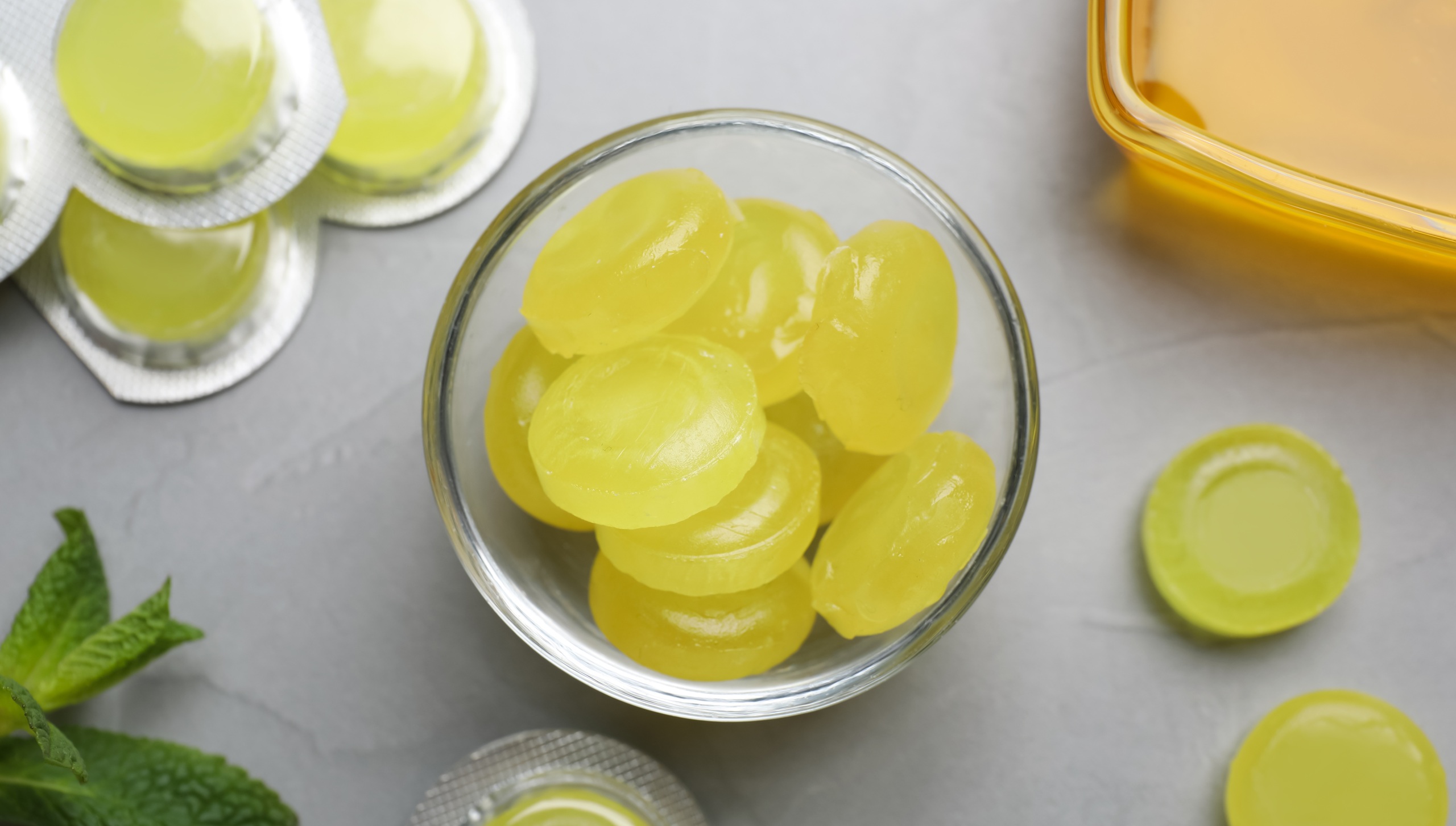 Many yellow cough drops, honey and mint on light grey background, top view