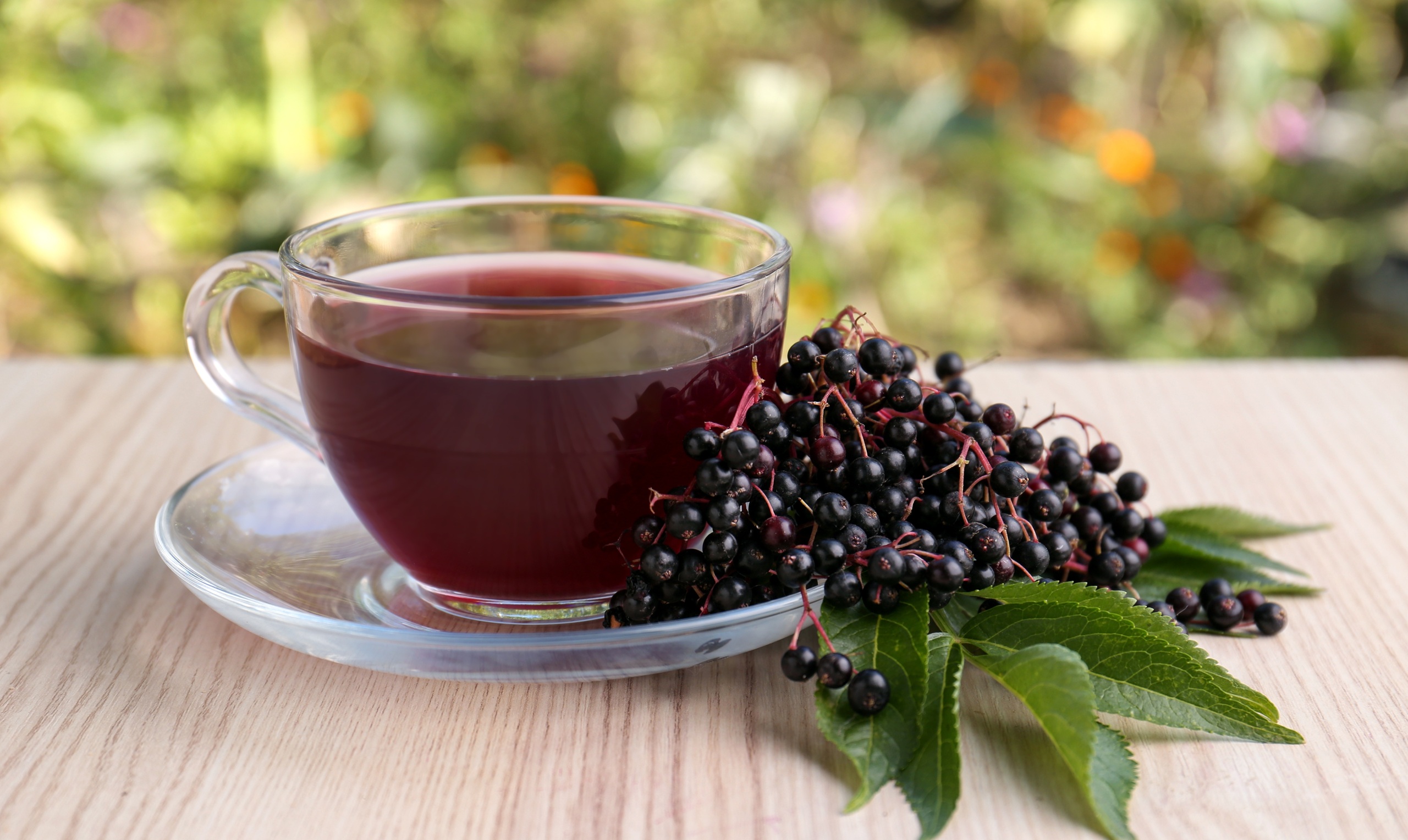 Glass cup of tasty elderberry tea and Sambucus berries on wooden table outdoors