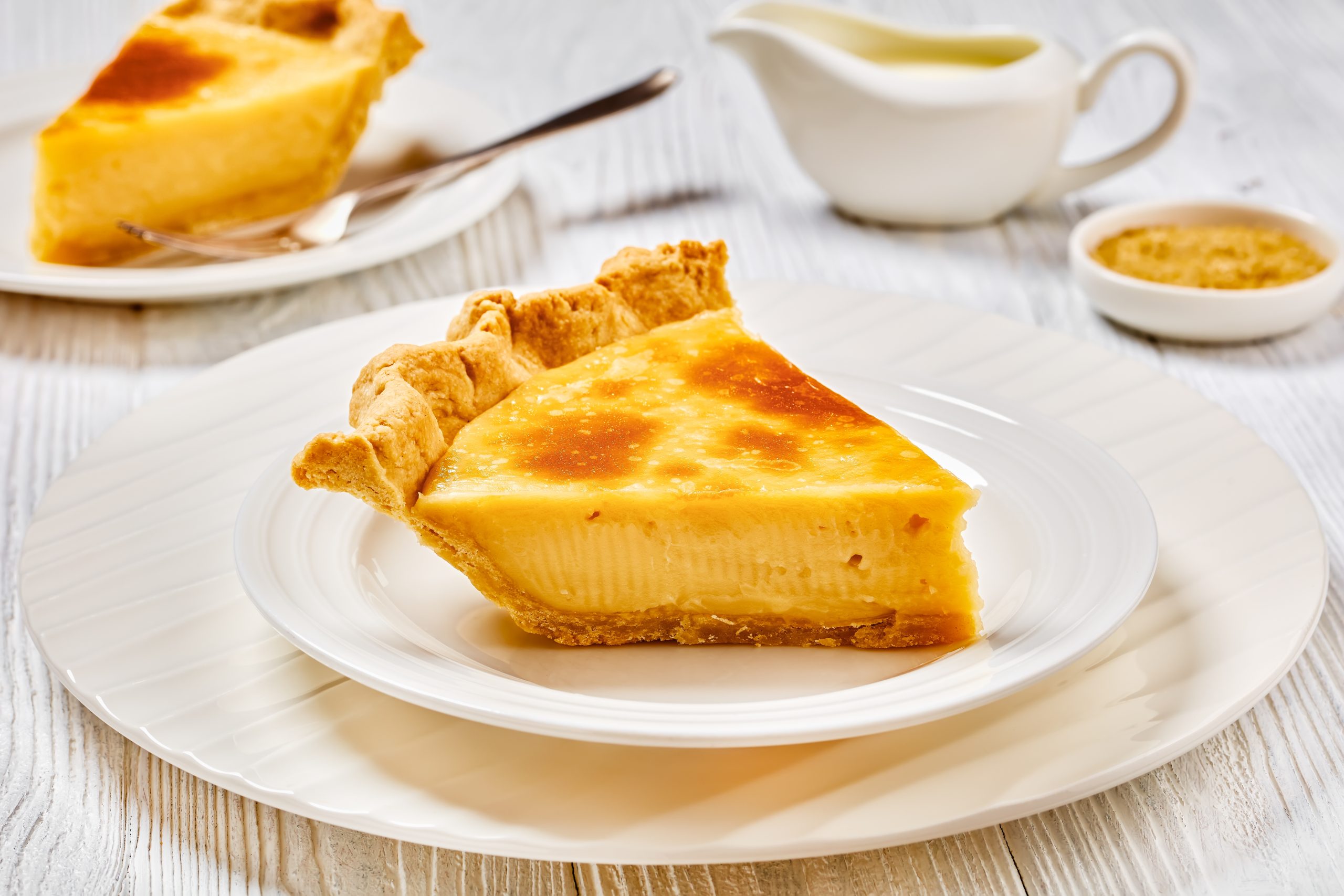 a slice of classic sugar cream pie, hoosier pie, indiana custard cream pie on white plate on white wood table