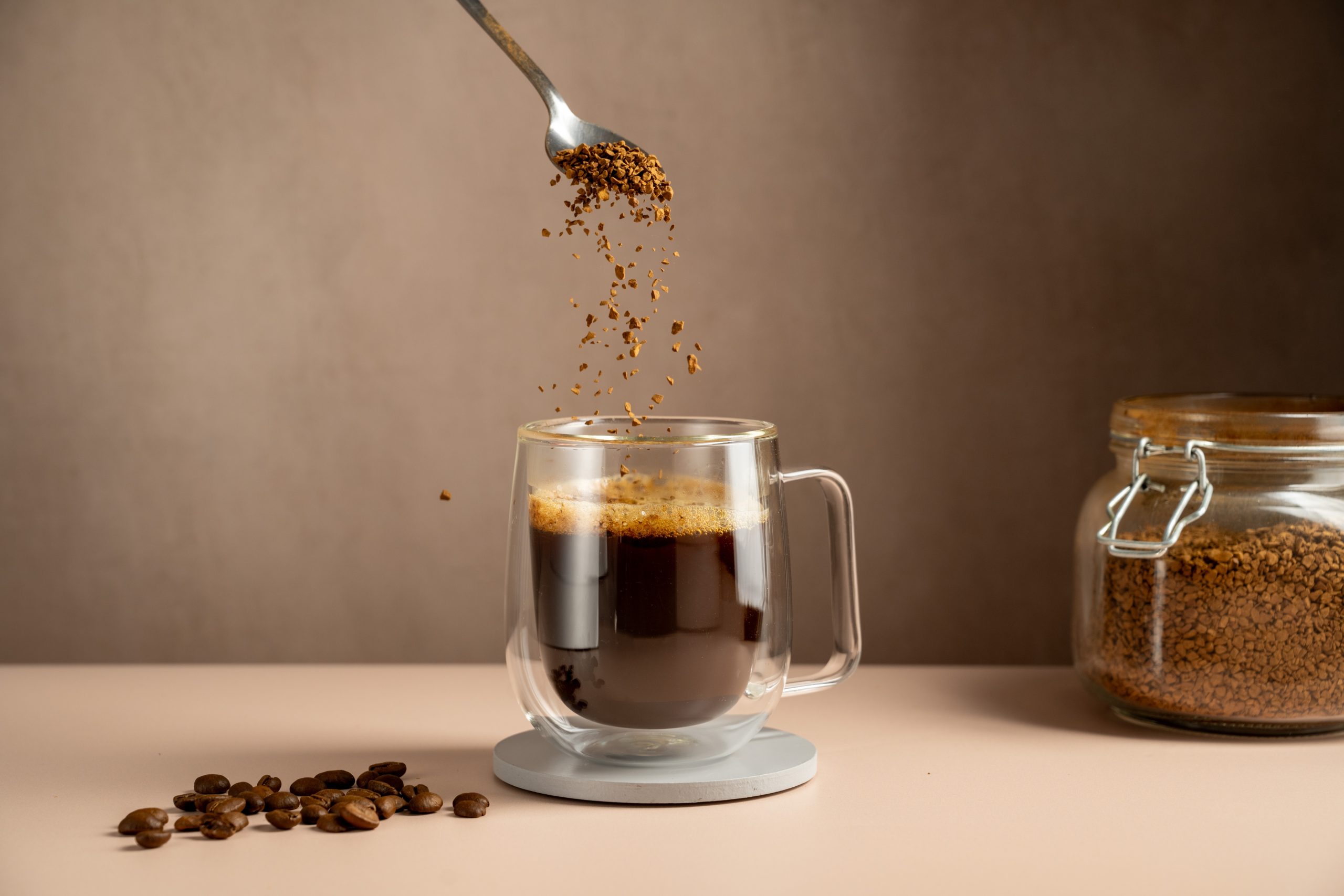 Instant coffee pouring in transparent glass mug, roasted coffee beans.