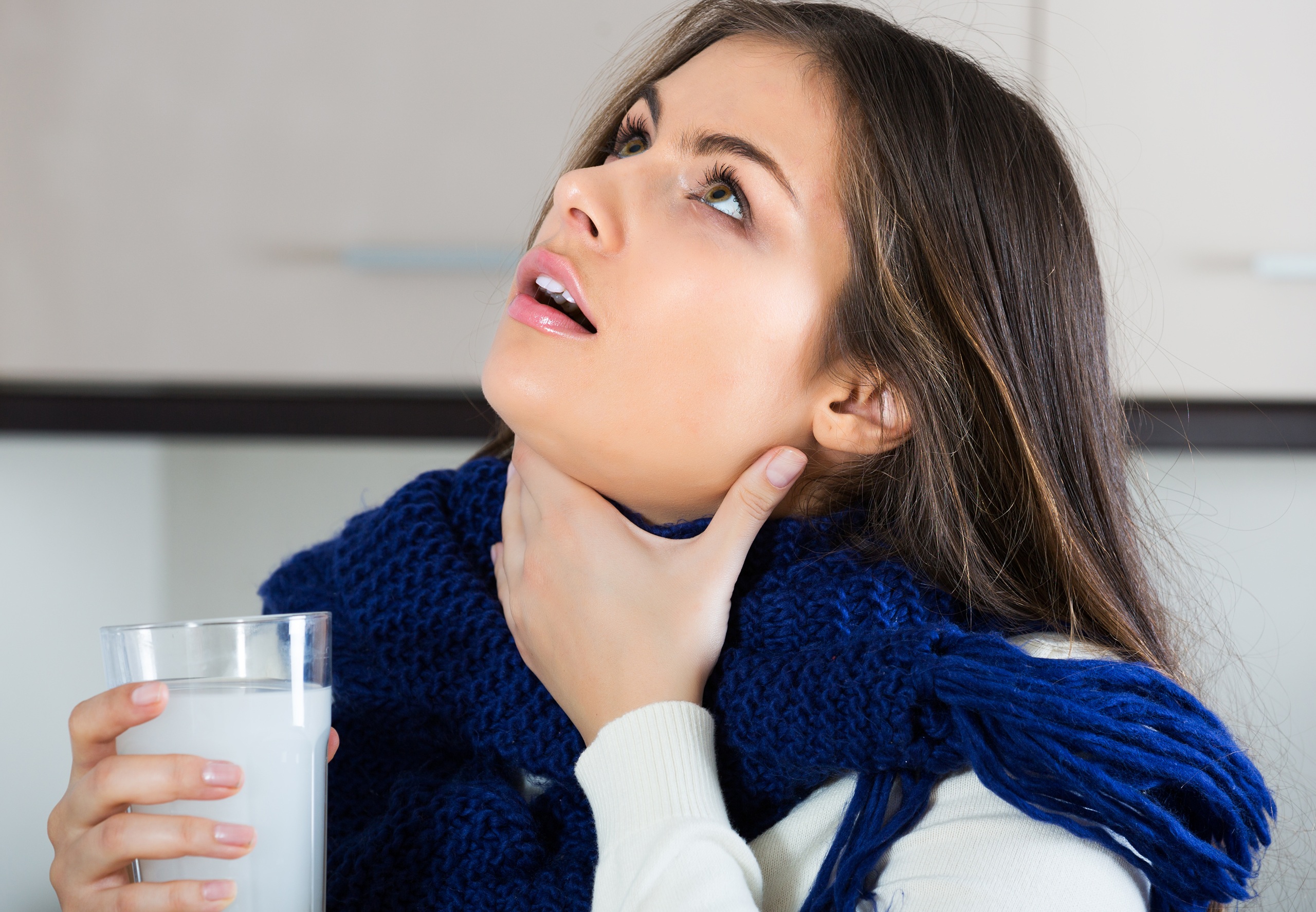 Young brunette woman in scarf gargling throat with medicine