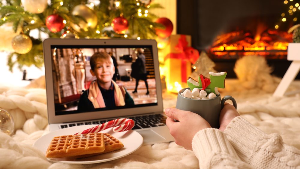 Woman with sweet drink watching Home Alone movie on laptop at home, closeup. Cozy winter holidays atmosphere
