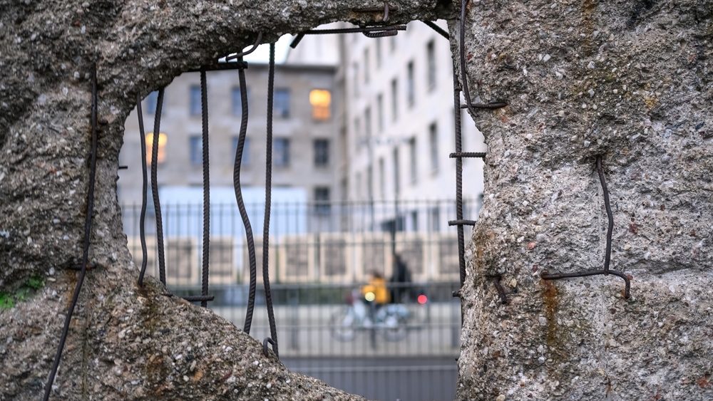 Bicyclists in the hole in Broken Berlin wall between East and west Berlin, symbol of the Cold War. Concept of freedom and independence.
