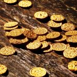 An array of lustrous gold coins spread out over a dark, aged wooden background, bathed in soft light that accentuates their rich textures and historic value.